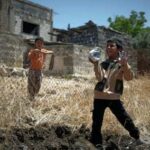 Ein Kind spielt mit den Überresten einer Mörsergranate, die die israelische Armee im Juni 2026 bei einem Überfall auf ein Dorf in der Provinz Daraa nahe der syrisch-jordanischen Grenze abgefeuert hatte. Ein Anwohner erzählte, als er israelische Soldaten fragte, warum sie seine Enkel im Teenageralter festnahmen, hätten diese geantwortet: „Die Kinder reden einfach zu viel.“ (Bildnachweis: Omar Sanadiki/AP)
